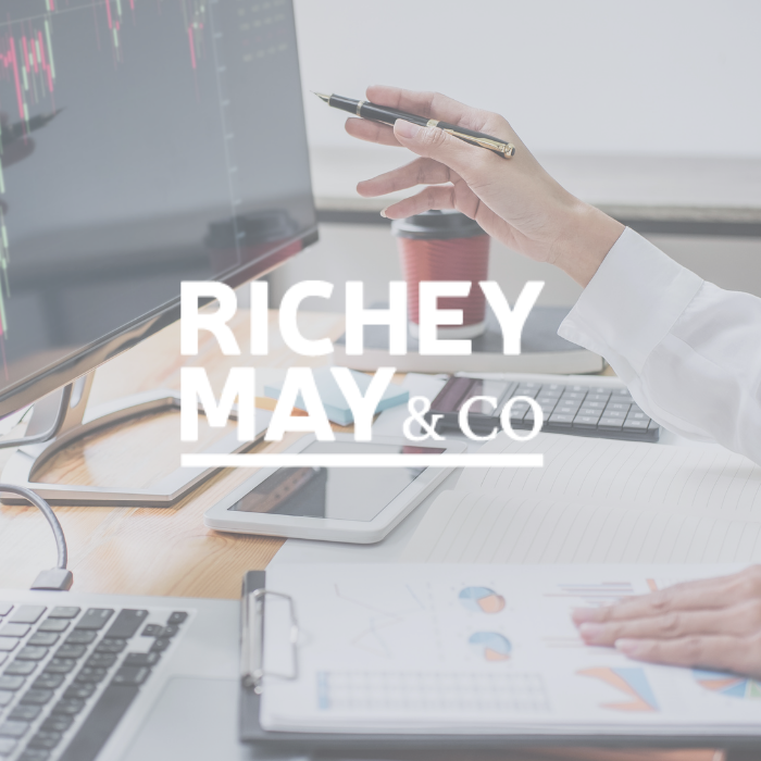 Richey May & Co title with background of a man sitting at a desk pointing toward his computer screen